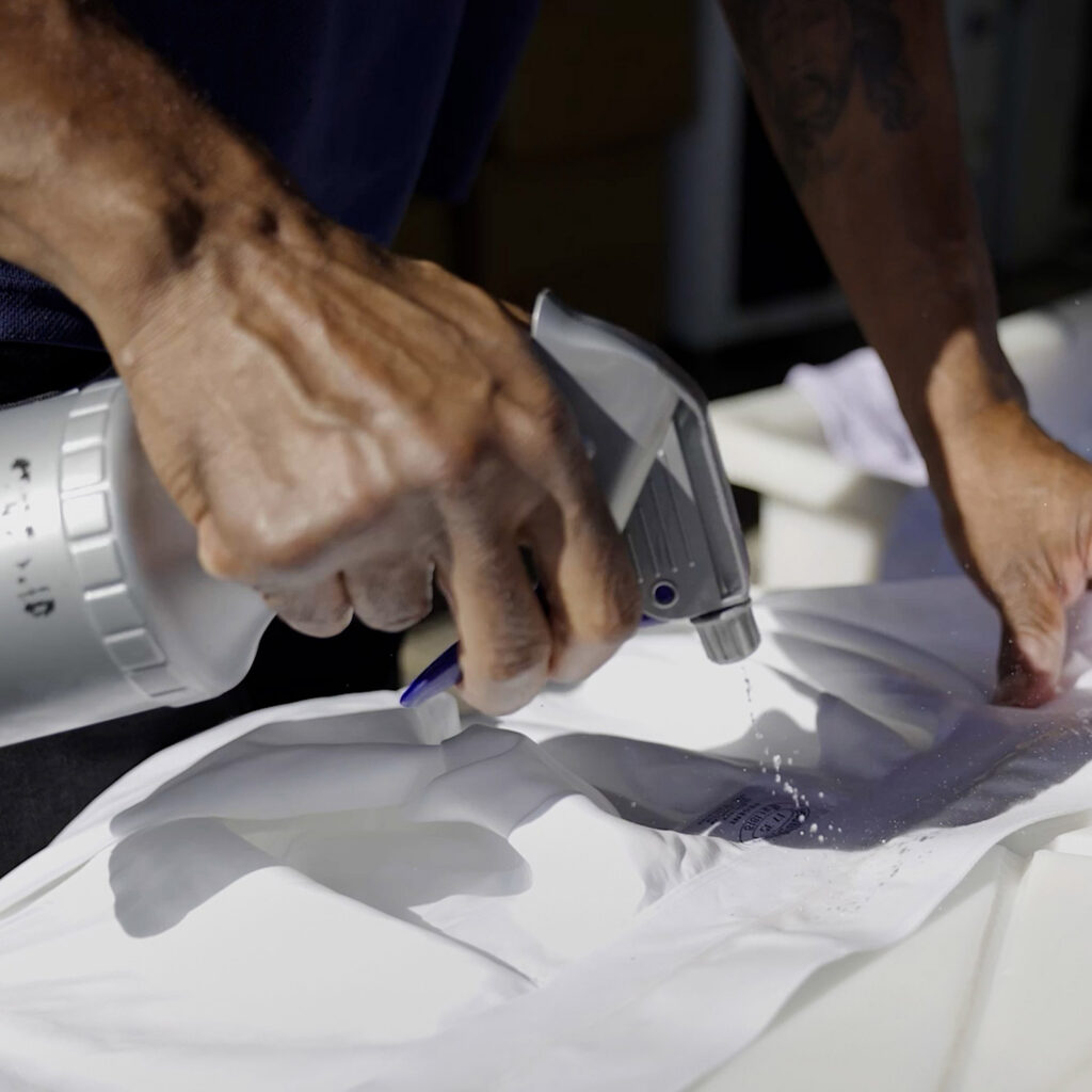 Technician applying targeted stain pre-treatment to a white shirt collar at Sudsies