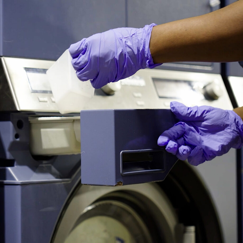 Sudsies team member loading professional dry cleaning machine with cleaning solution