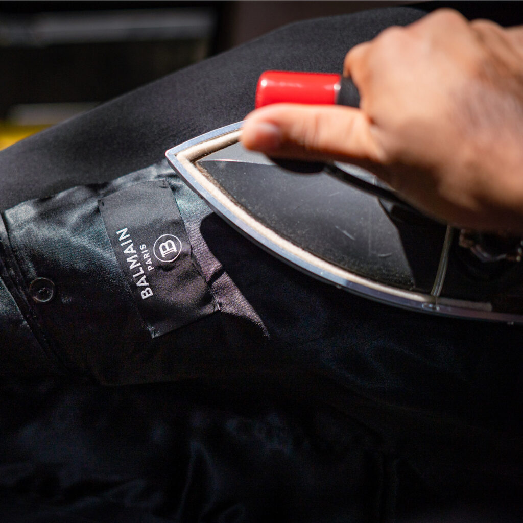 Sudsies specialist pressing a luxury designer garment during professional finishing process